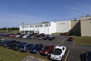 Large industrial building marked "BioVectra" with adjacent parking lot filled with various cars under a clear blue sky.