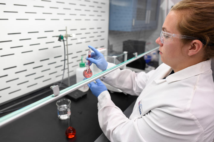 A person in a lab coat conducts an experiment in a laboratory, using flasks and protective gear, indicating a focus on scientific research.