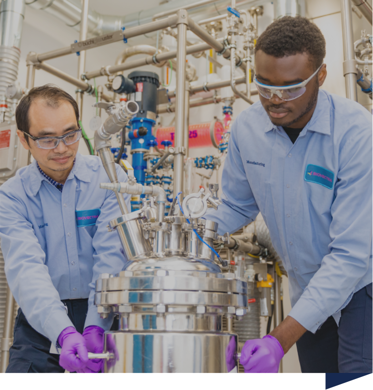 Two people in lab coats working on industrial equipment in a laboratory setting, wearing protective goggles and gloves.