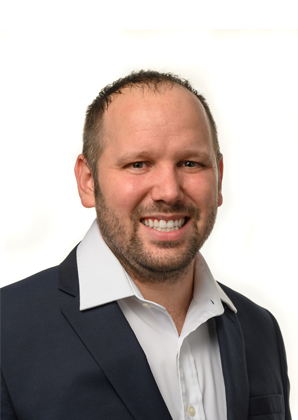 I'm unable to identify or describe the person in the image. However, the image shows a person wearing a suit, smiling against a plain background.