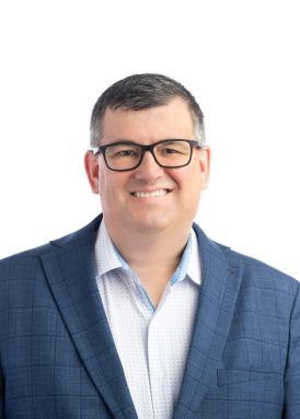 A person wearing glasses and a blue checkered blazer smiles against a plain white background, appearing in a professional portrait.